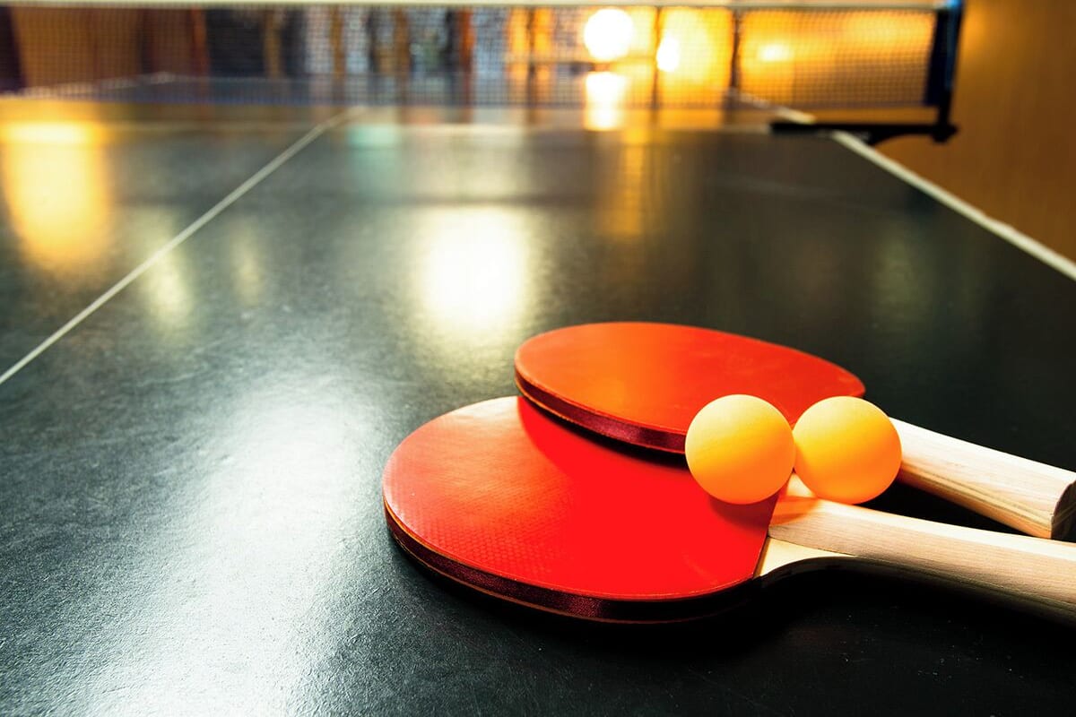 A table tennis table with two red paddles and two yellow balls.