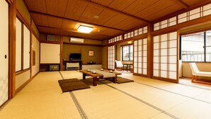 A traditional Japanese room with tatami flooring, a low table with cushions, sliding doors, and a television. - Kinosaki Onsen Restaurant & Ryokan Yoshiharu (Toyooka)