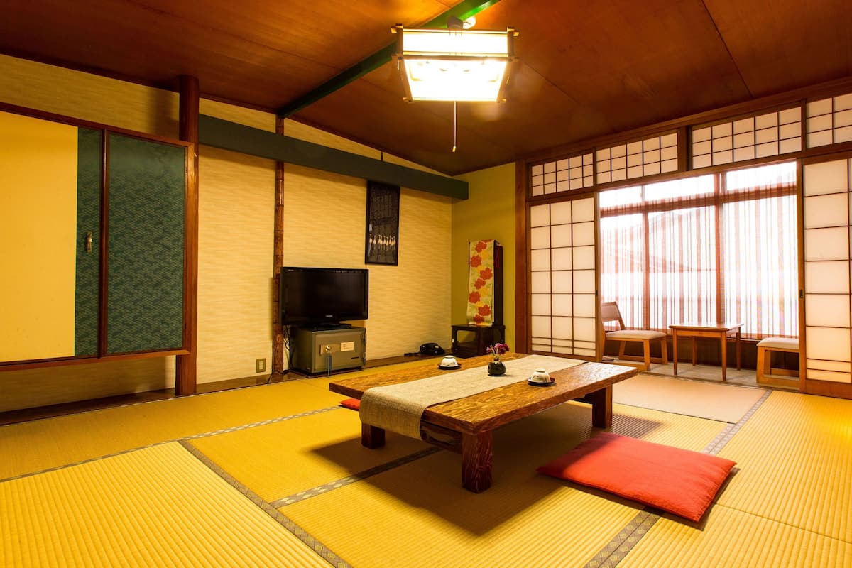 A traditional Japanese room with tatami flooring, a low table, a television, and sliding doors.