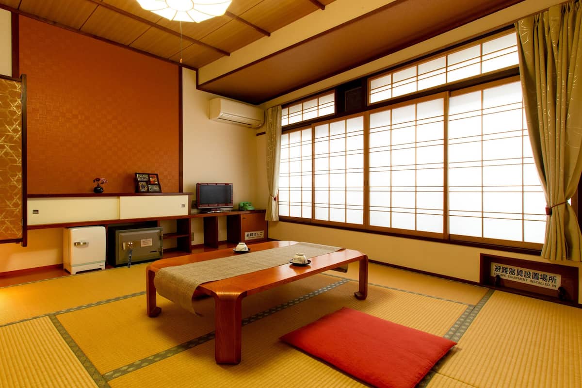 A traditional Japanese room with tatami flooring, a low wooden table, a television, and a futon bed.