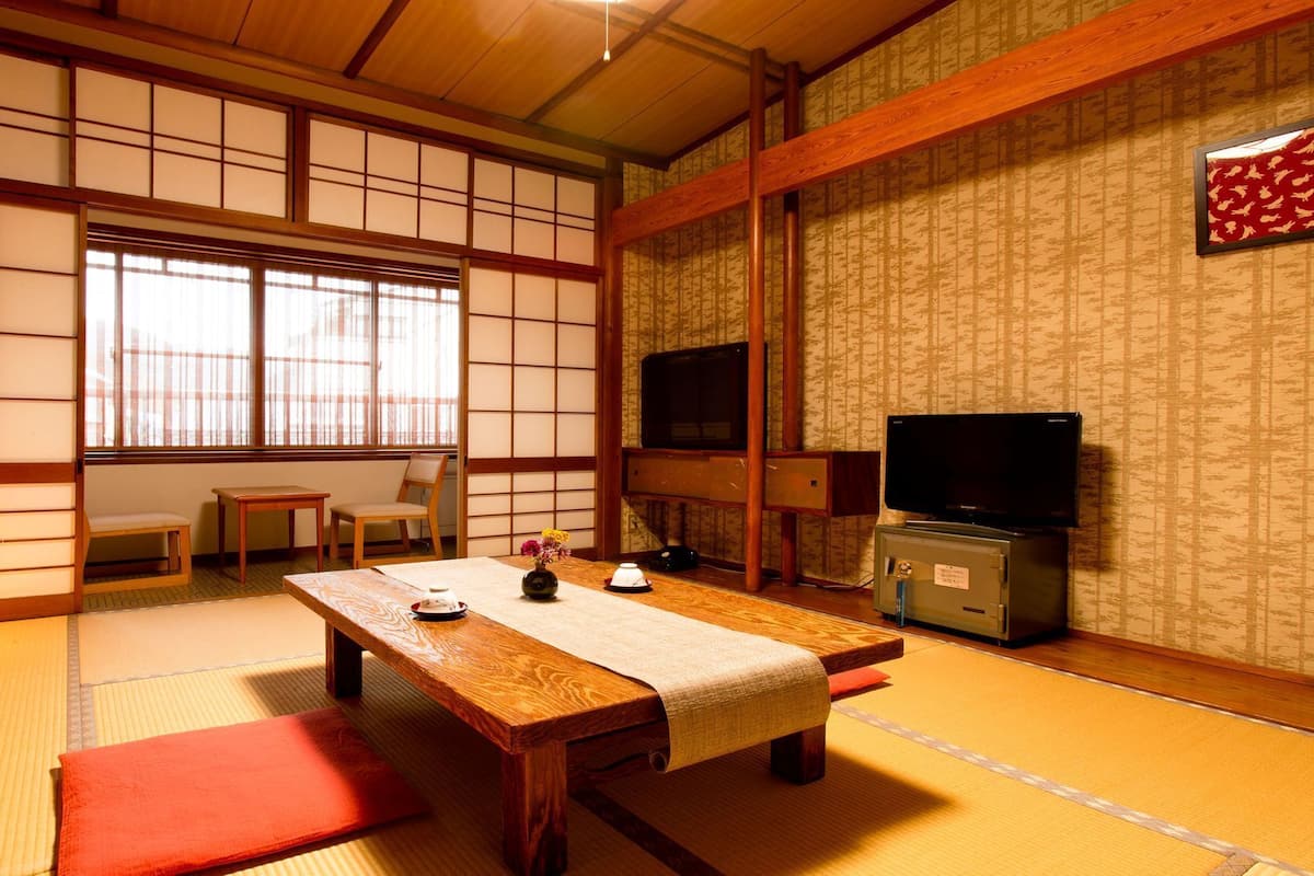 A traditional Japanese room with tatami flooring, a low wooden table, a television, and a sliding door.