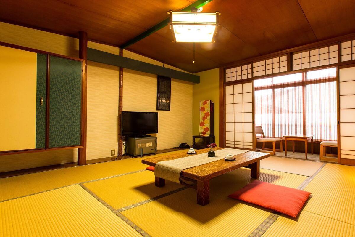 A traditional Japanese room with tatami flooring, a low wooden table, a television, and sliding doors.