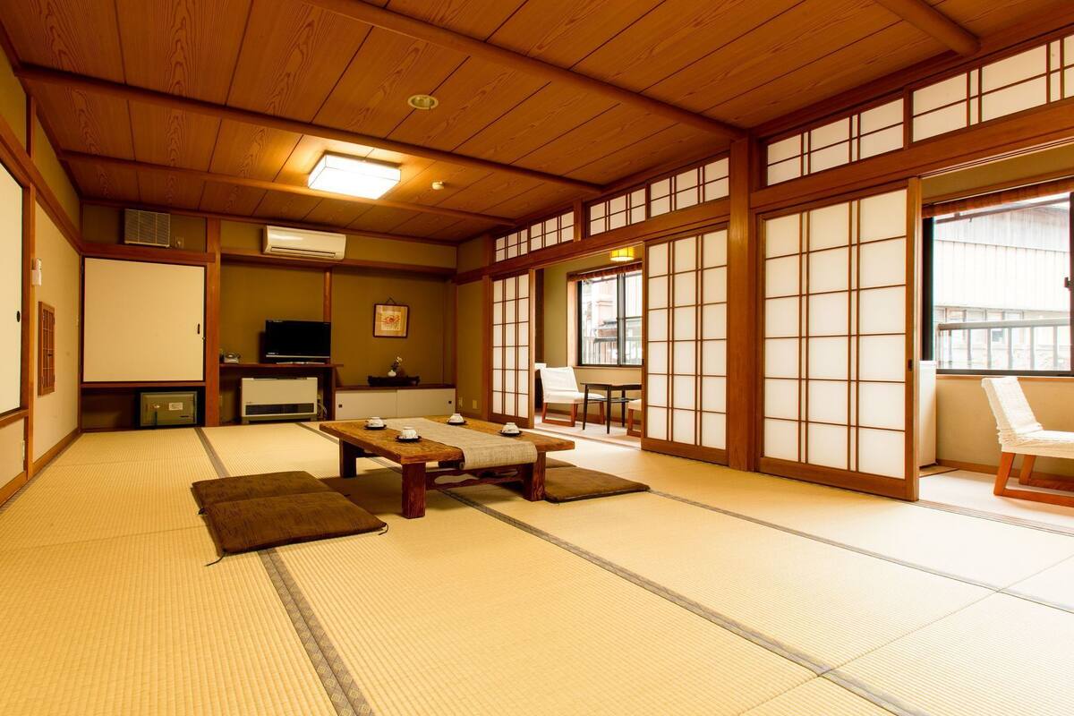 A traditional Japanese room with tatami flooring, a low table with cushions, a television, and sliding doors.