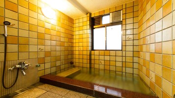 Casa de banho com paredes em azulejos amarelos, uma banheira, um chuveiro e uma janela.
