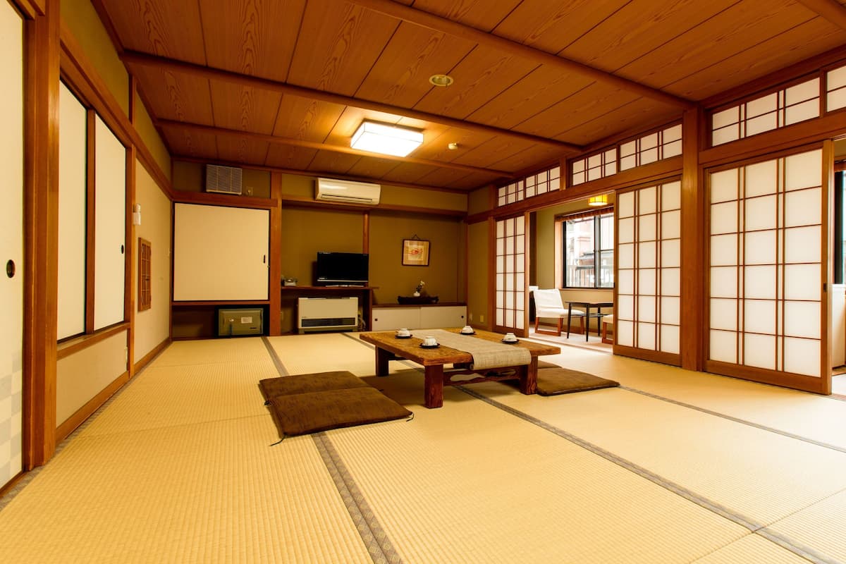 A traditional Japanese room with tatami flooring, a low table with cushions, sliding doors, and a television.