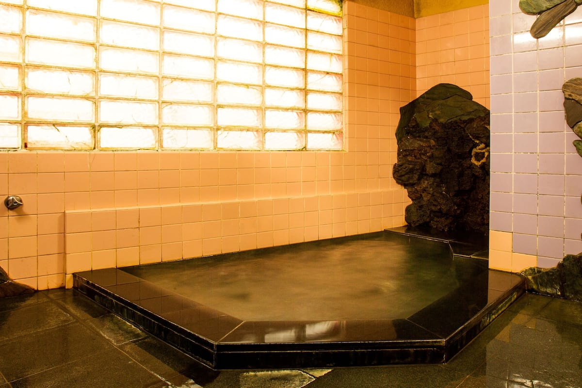 A small, dark-colored room with a tiled floor, a stone wall, and a window with a grid pattern.