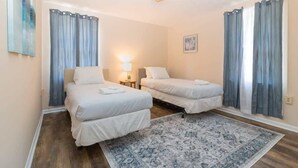 A hotel room with two beds, a patterned rug, and curtains. - Modern Interior - Delightful Doubles Unit D (Columbus)