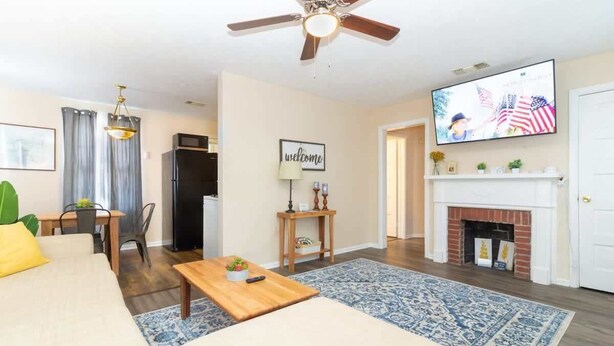 A living room with a sofa, coffee table, TV, fireplace, and a ceiling fan. - Modern Interior - Delightful Doubles Unit D (Columbus)