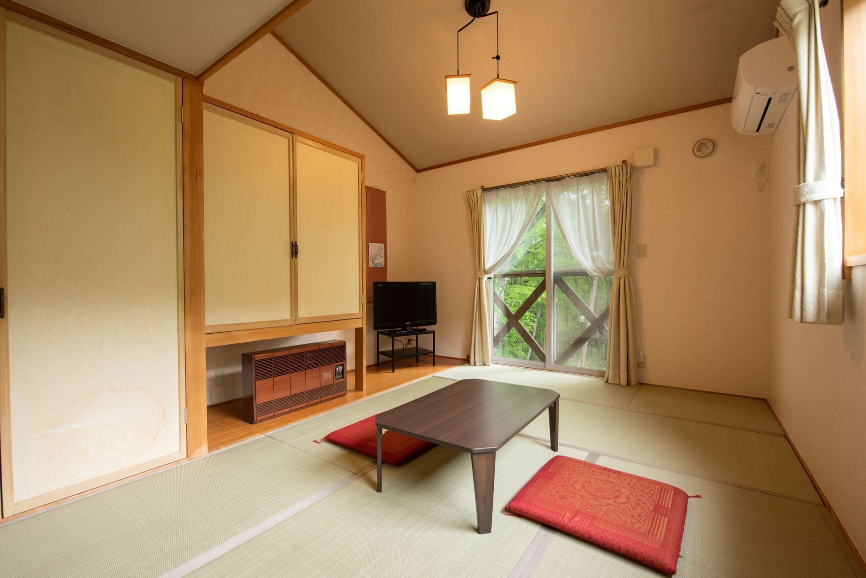 A traditional Japanese-style room with tatami flooring, a low table, a television, and sliding doors.