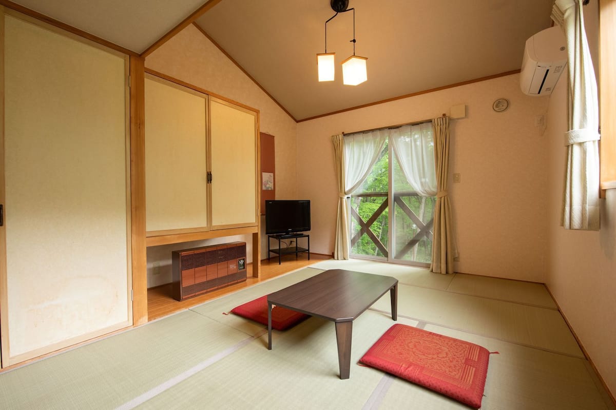 Ein traditioneller japanischer Raum mit Tatami-Böden, einem niedrigen Tisch, einem Fernseher und Schiebetüren.