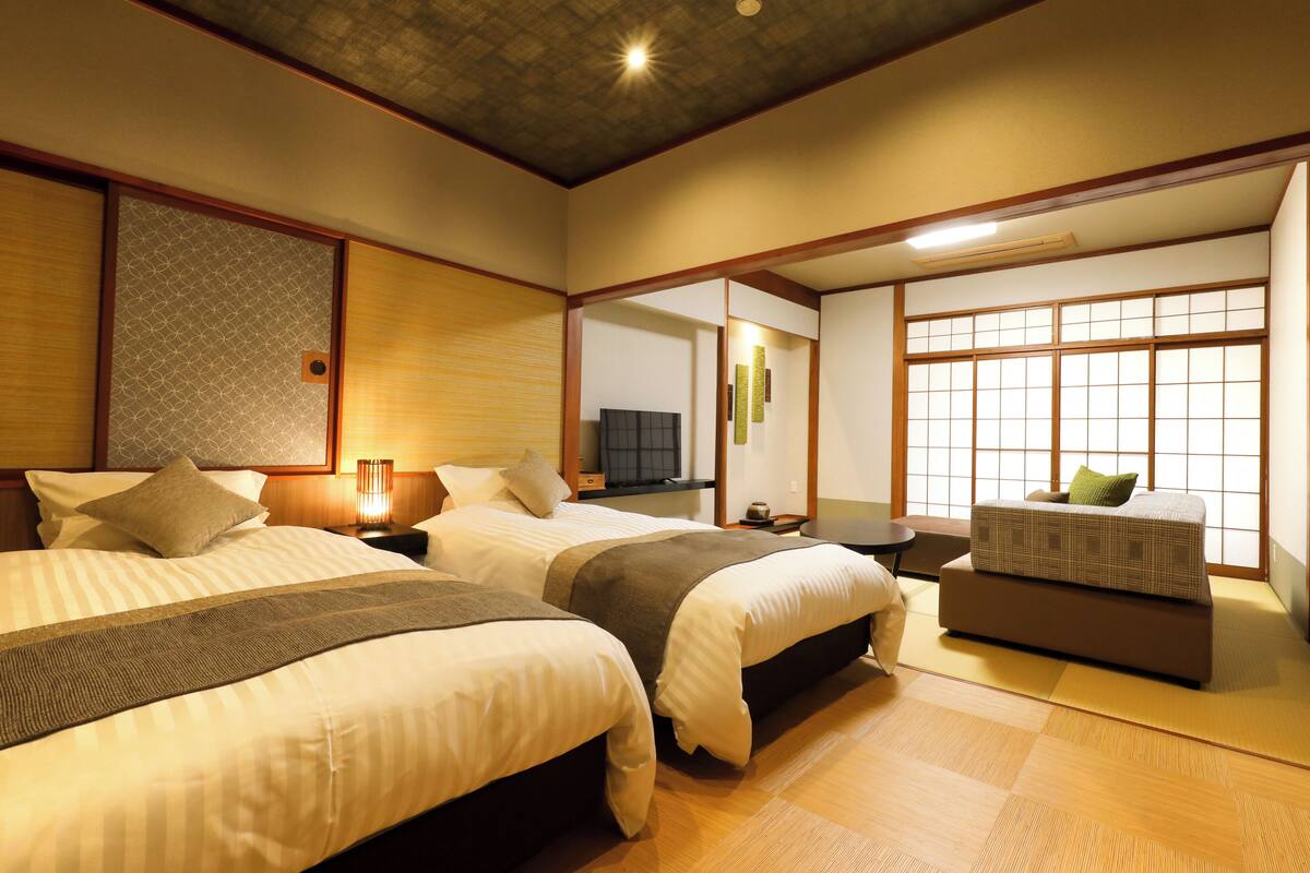 A hotel room with two beds, a sofa, a TV, and a large window.