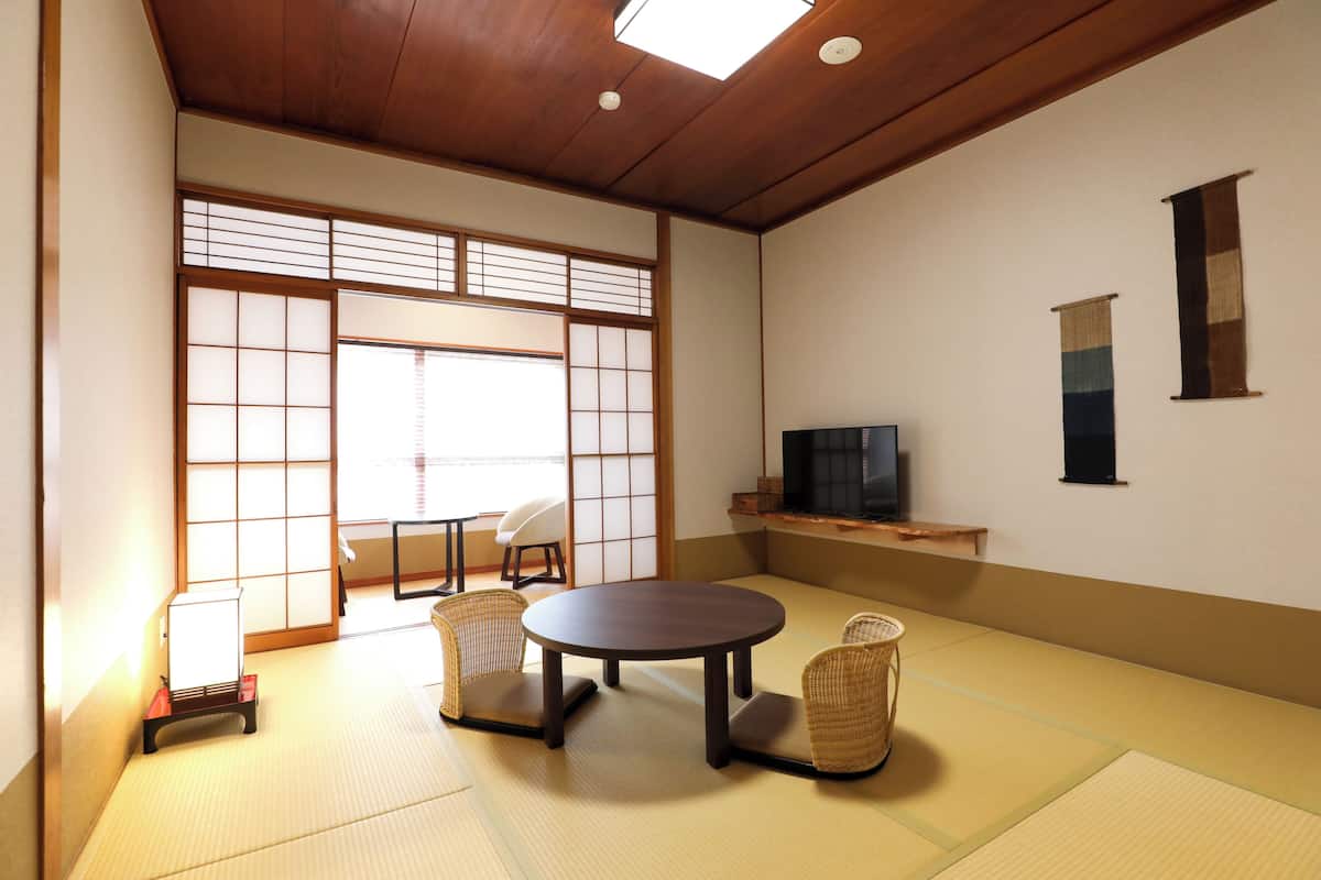 A traditional Japanese room with tatami flooring, a low table, two chairs, a television, and sliding doors.