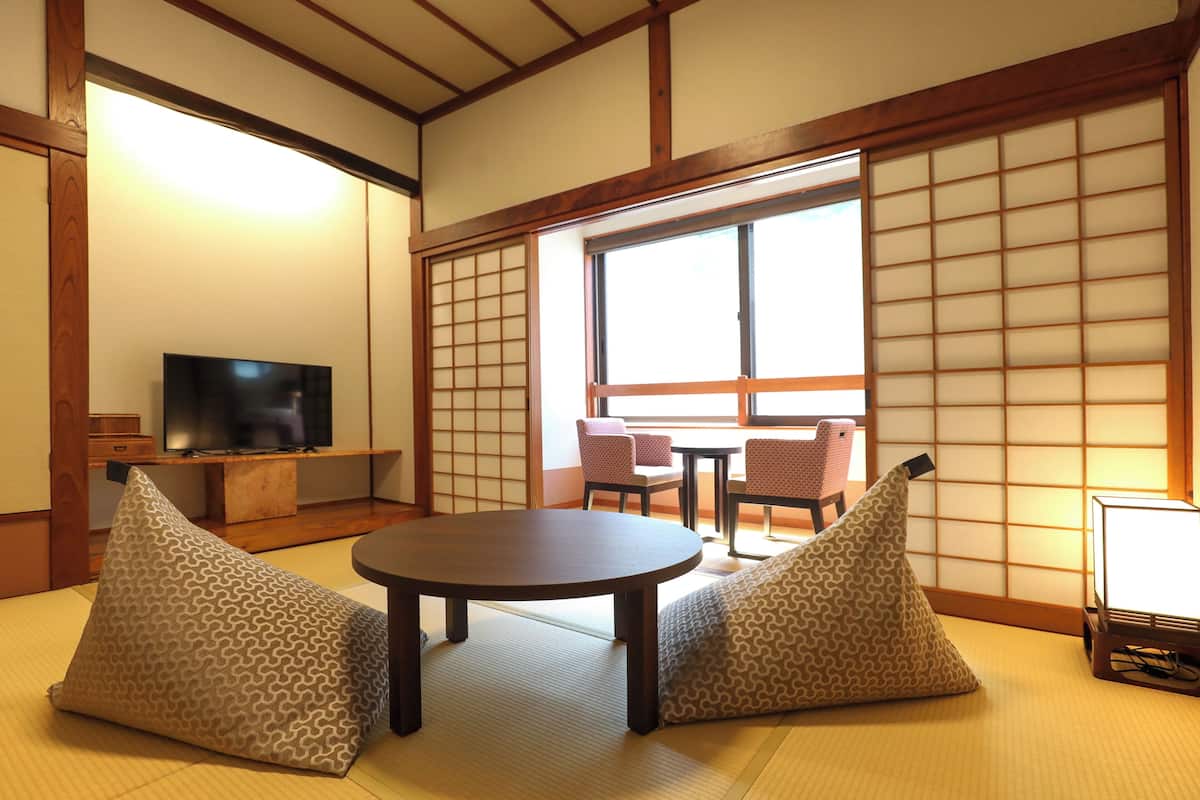 A traditional Japanese room with tatami flooring, a low table, cushions, a television, and sliding doors.