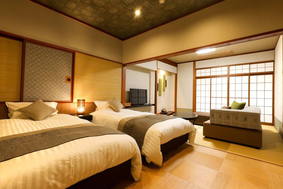 A traditional Japanese-style hotel room with two beds, a small sofa, a television, and sliding doors.