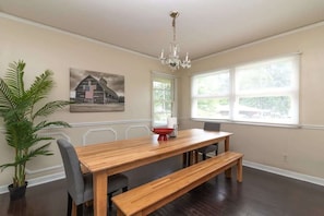 A dining area with a wooden table, benches, a chandelier, a potted plant, and a wall-mounted picture of a barn. - 10 Min to Downtown, Close to Dining-Boxwood Beauty (Columbus)