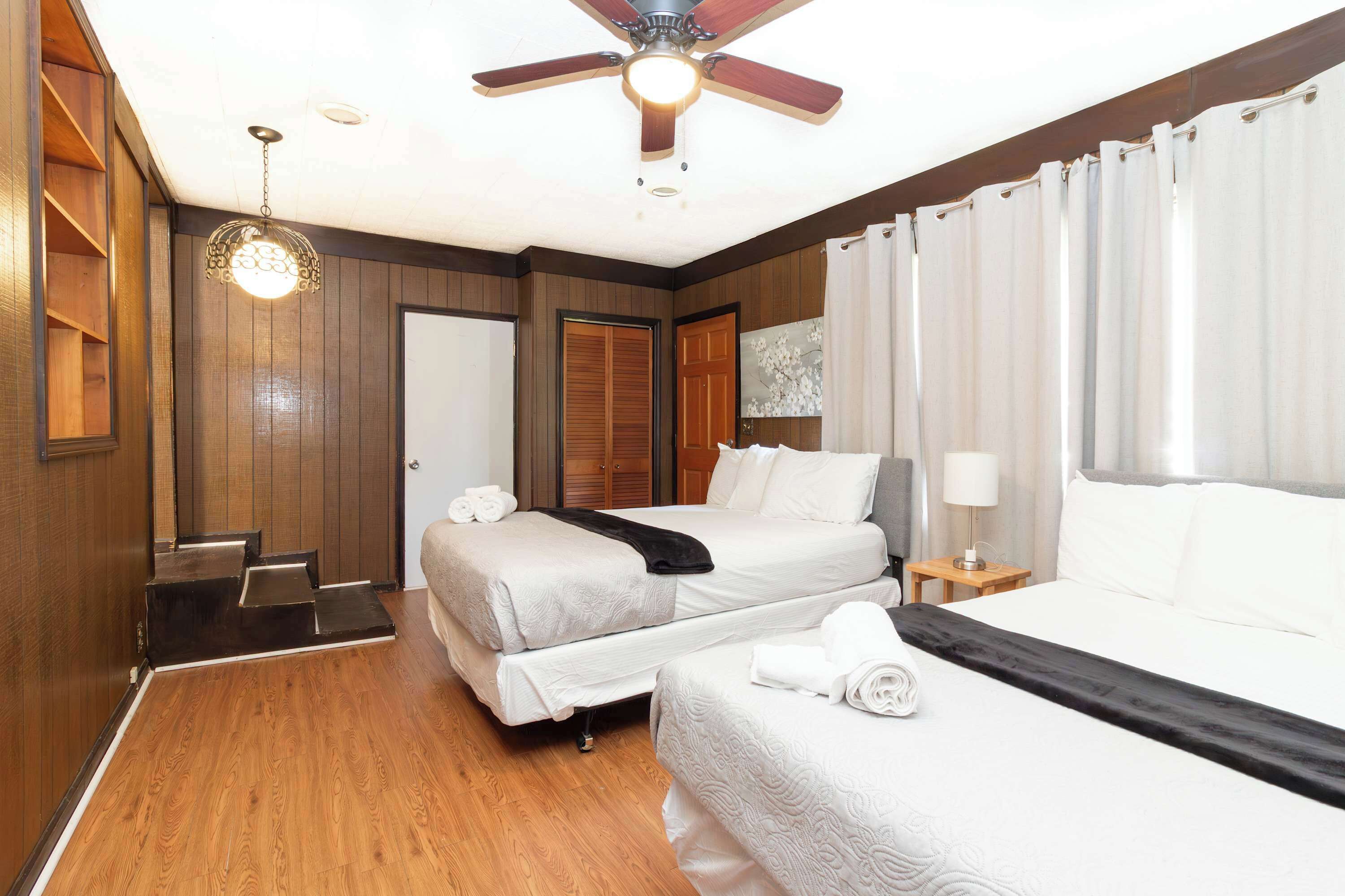 Ein Hotelzimmer mit zwei Betten, einem Deckenventilator, Holzboden und einem Holzschrank.