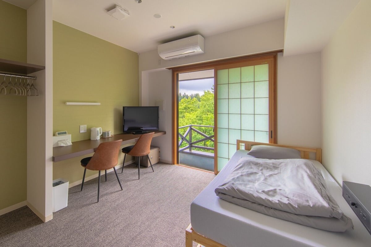 Quarto com cama, escrivaninha com cadeira, televisão e varanda com vista.
