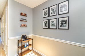 A hallway with framed black and white photographs on the wall, a signboard, and a shelf with items.