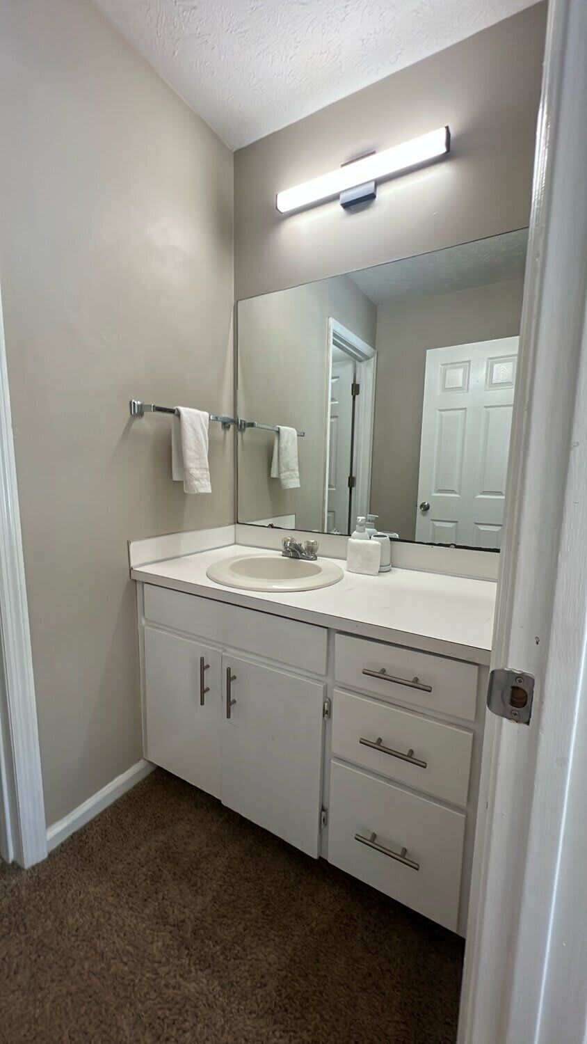 A bathroom with a white sink, mirror, and cabinets.