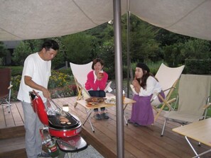 Un groupe de personnes se trouve à l’extérieur, près d’un barbecue, d’une table et de chaises.