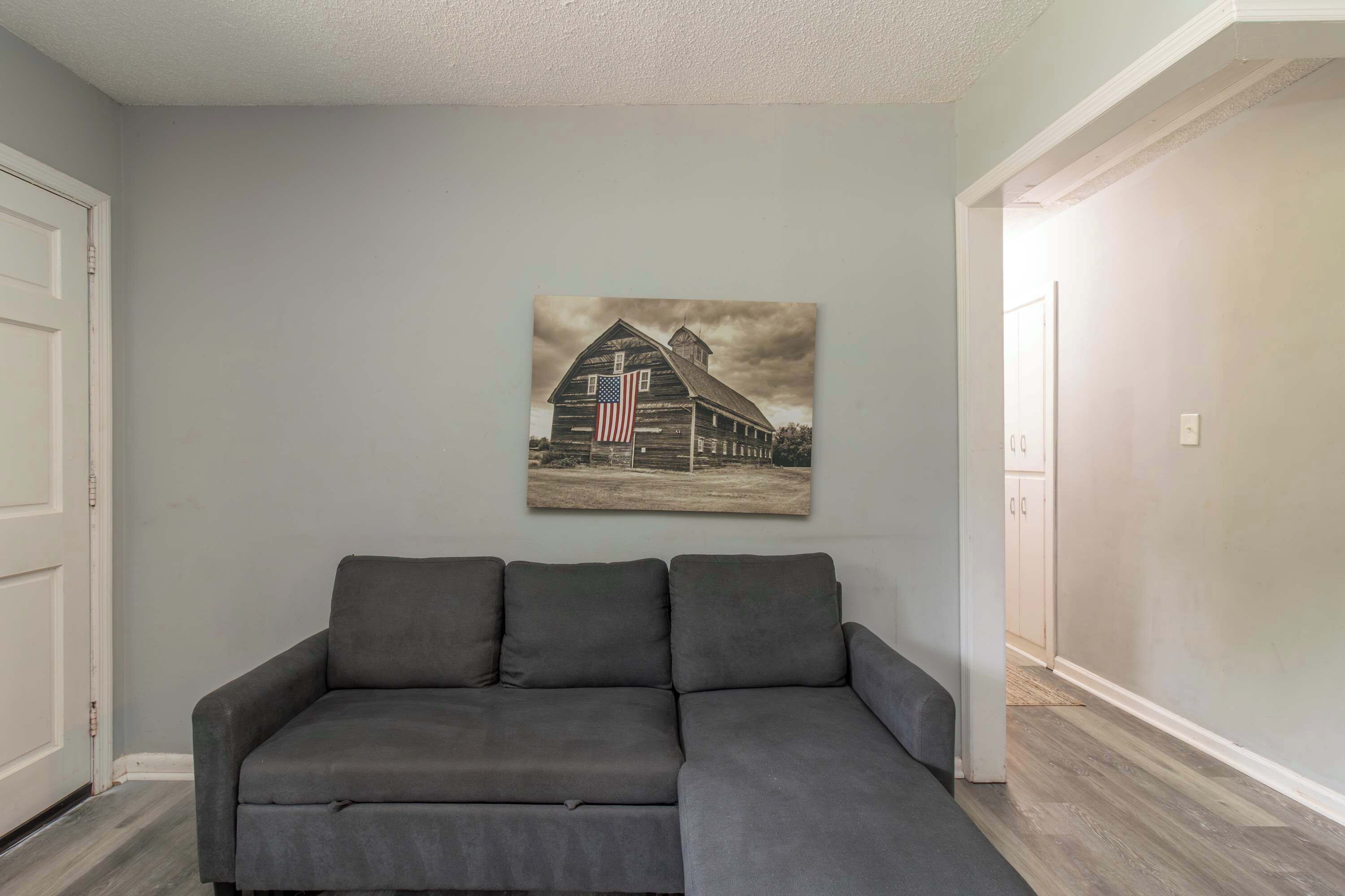 En grå modulsofa foran en lysegrå væg, med et billede af et lade og et amerikansk flag i ramme.