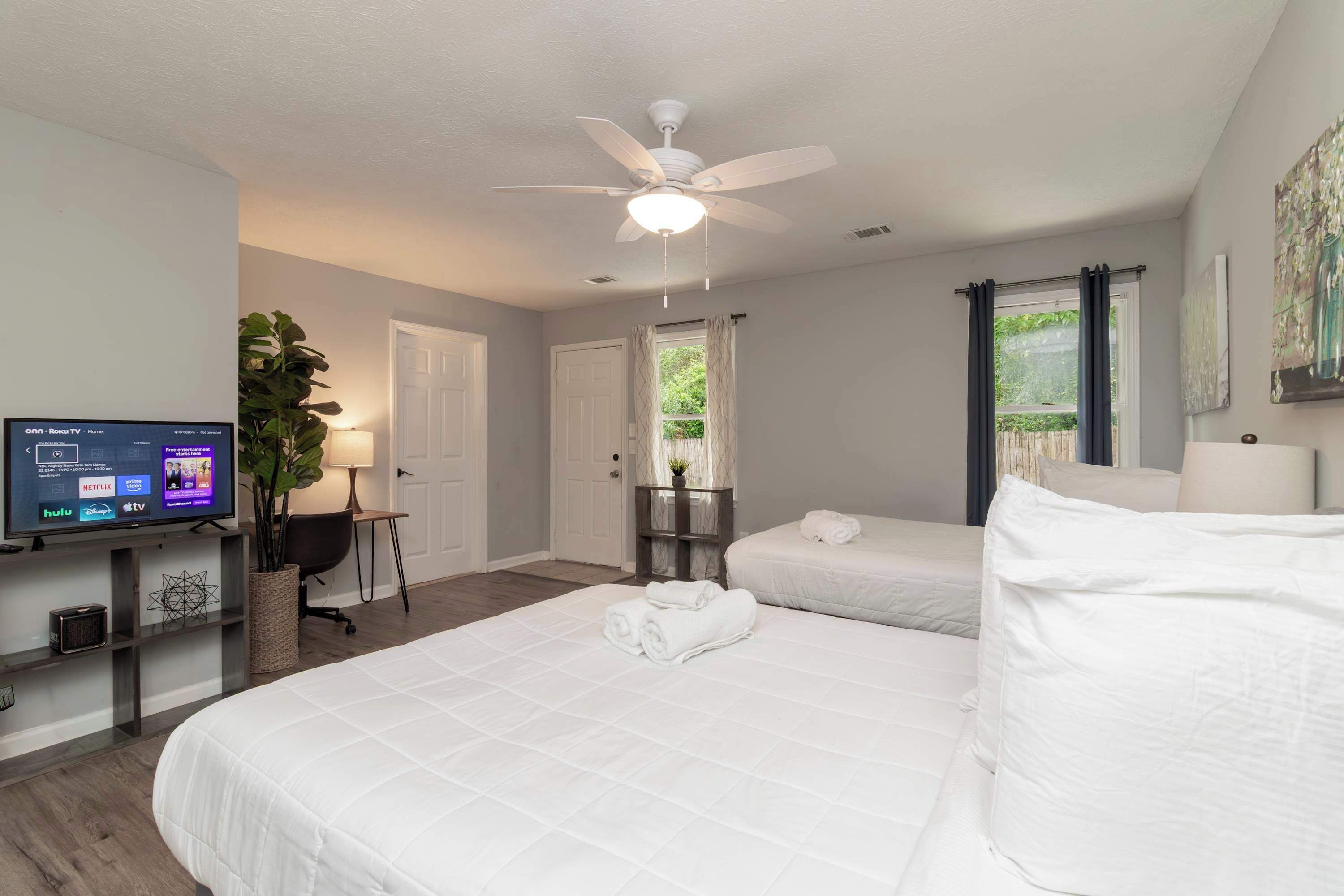 Habitación de hotel con cama, televisor, ventilador de techo y ventana con cortinas.