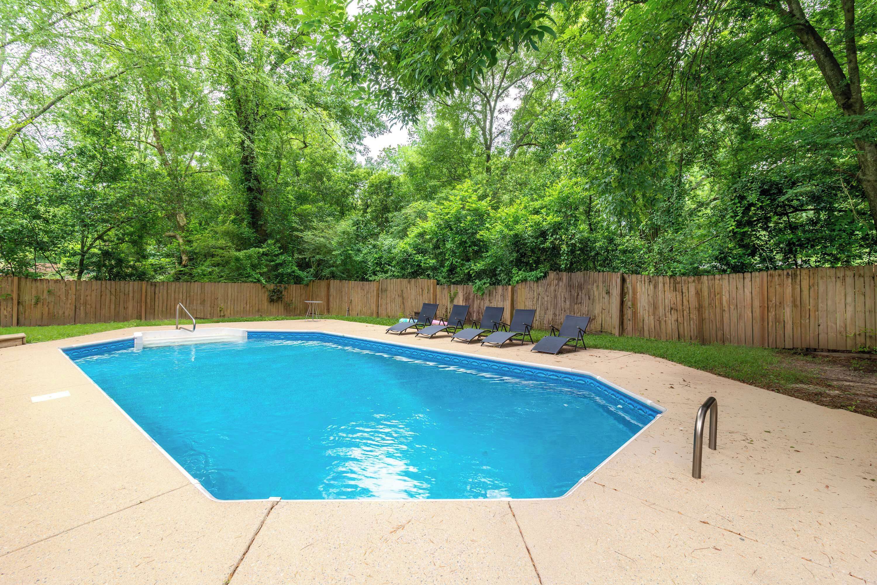 A rectangular swimming pool with a wooden fence and lounge chairs around it.