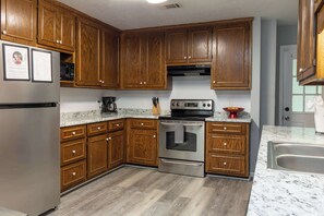 Cocina con gabinetes de madera, electrodomésticos de acero inoxidable y encimera de granito.