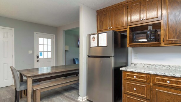 A kitchen with wooden cabinets, a stainless steel refrigerator, a microwave, and a dining table with chairs. - Pool, Fenced Yard, & Patio! Ventura Vista Retreat (Columbus)