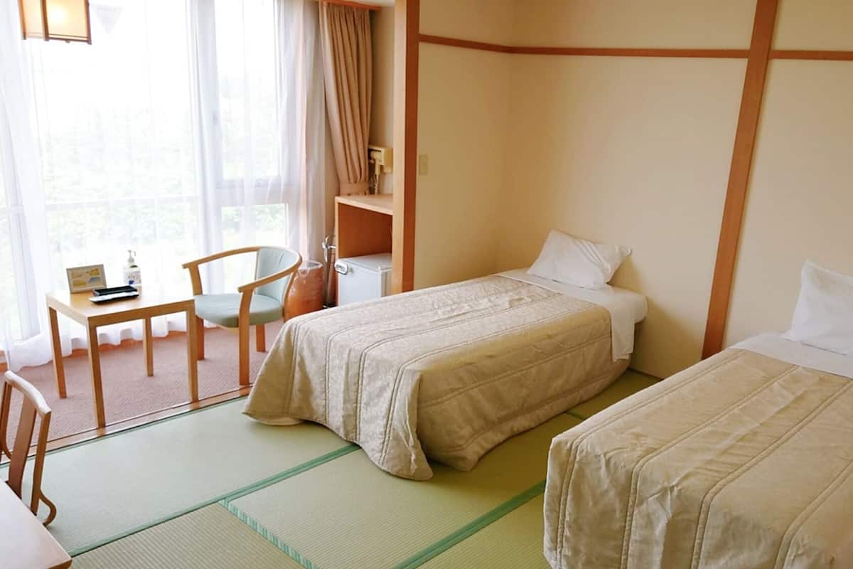 Camera d'albergo con due letti, una scrivania, una sedia e una finestra con tende.