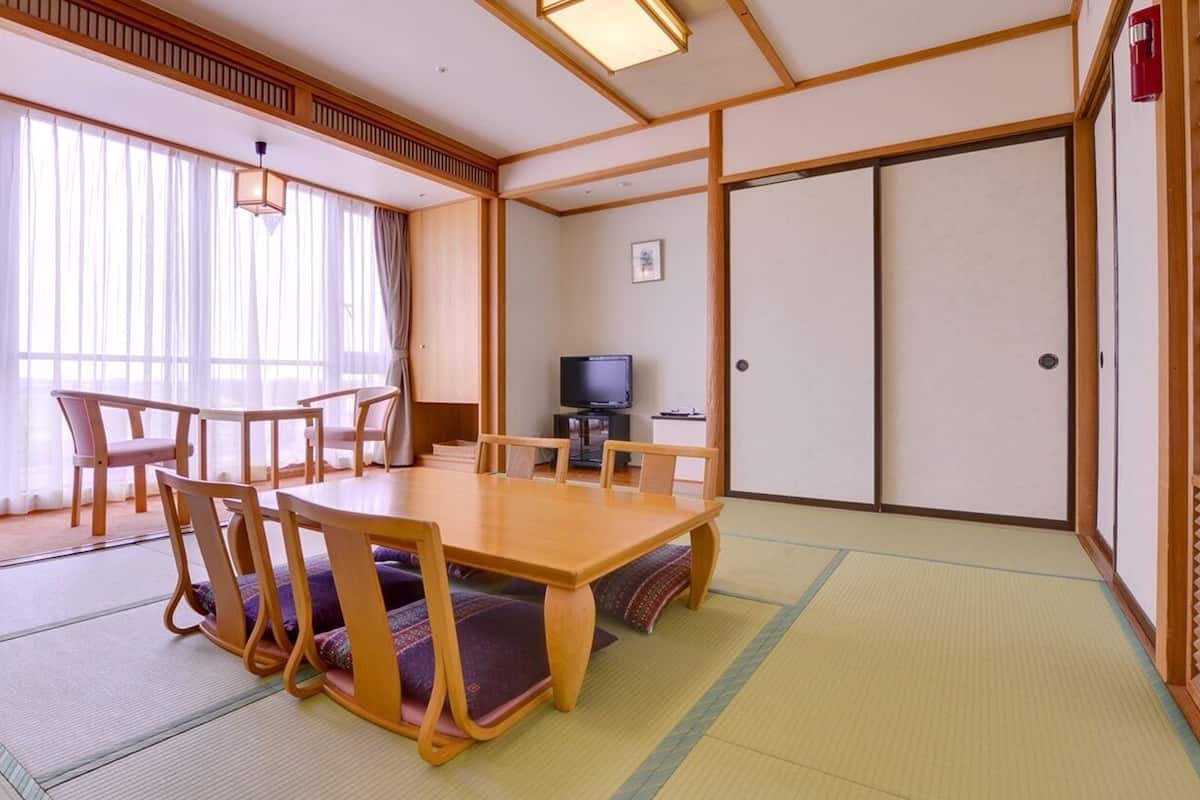 Una tradizionale stanza in stile giapponese con pavimento in tatami, un tavolo da pranzo in legno con sedie, un televisore e porte scorrevoli.