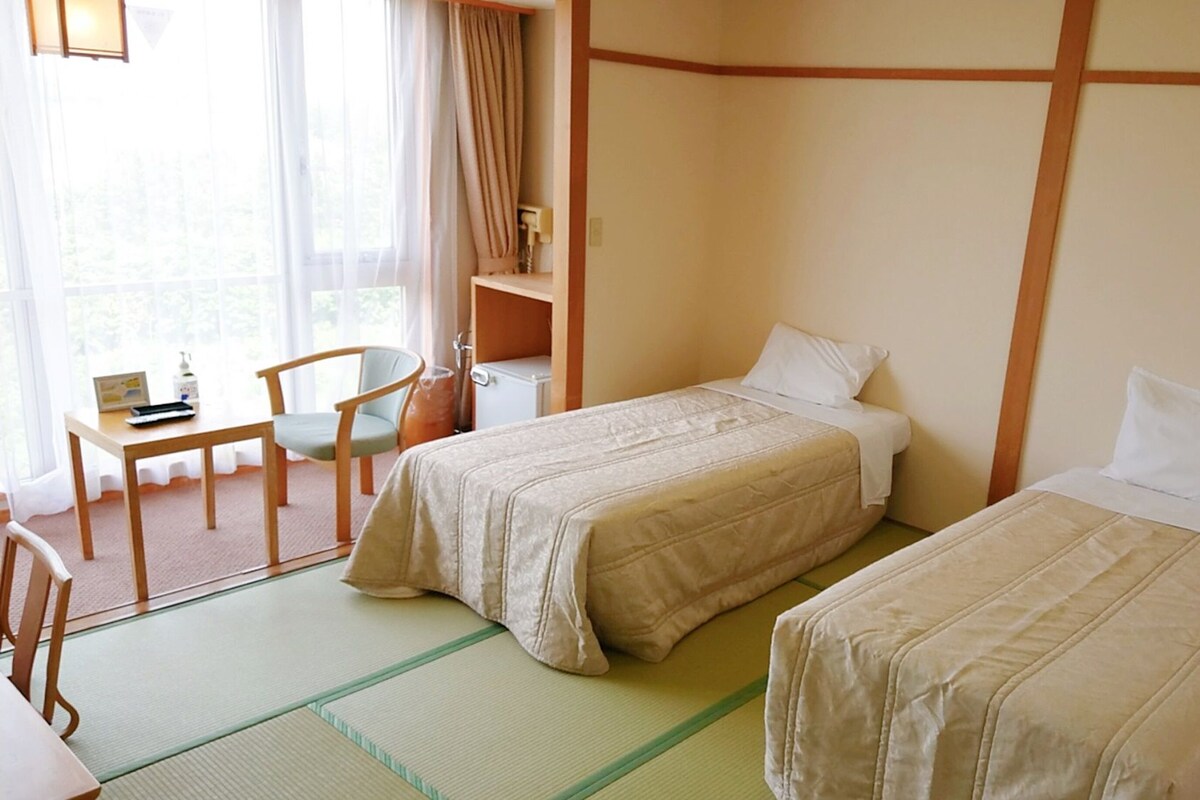 Ein Hotelzimmer mit zwei Betten, einem Schreibtisch, einem Stuhl und einem Fenster mit Vorhängen.