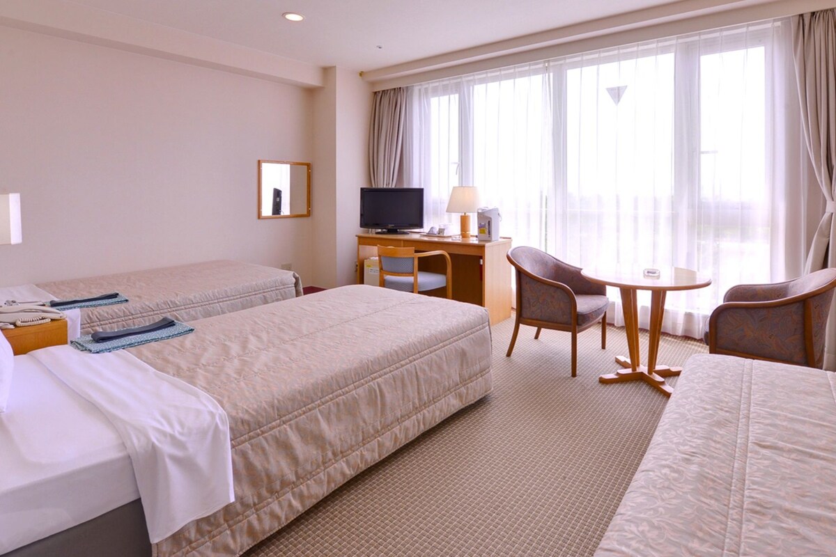 Une chambre d’hôtel avec deux lits, un bureau avec une télévision, une chaise et une petite table.