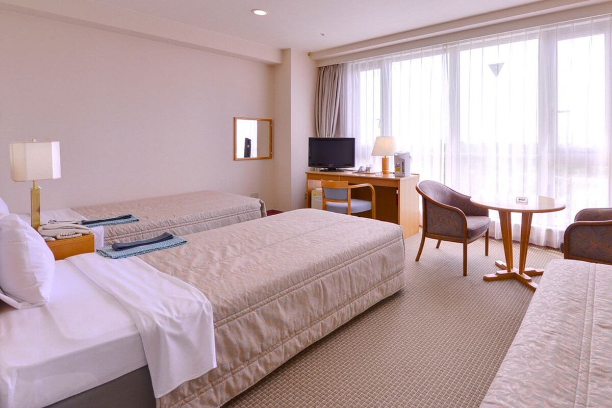 Ein Hotelzimmer mit zwei Betten, einem Schreibtisch mit Computer, einem Stuhl und einem kleinen Tisch.