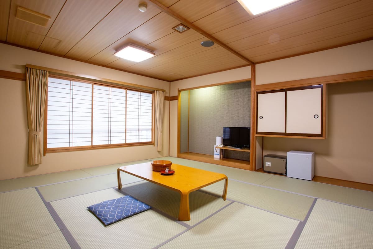 A tatami mat room with a low wooden table, a television, and a small refrigerator.