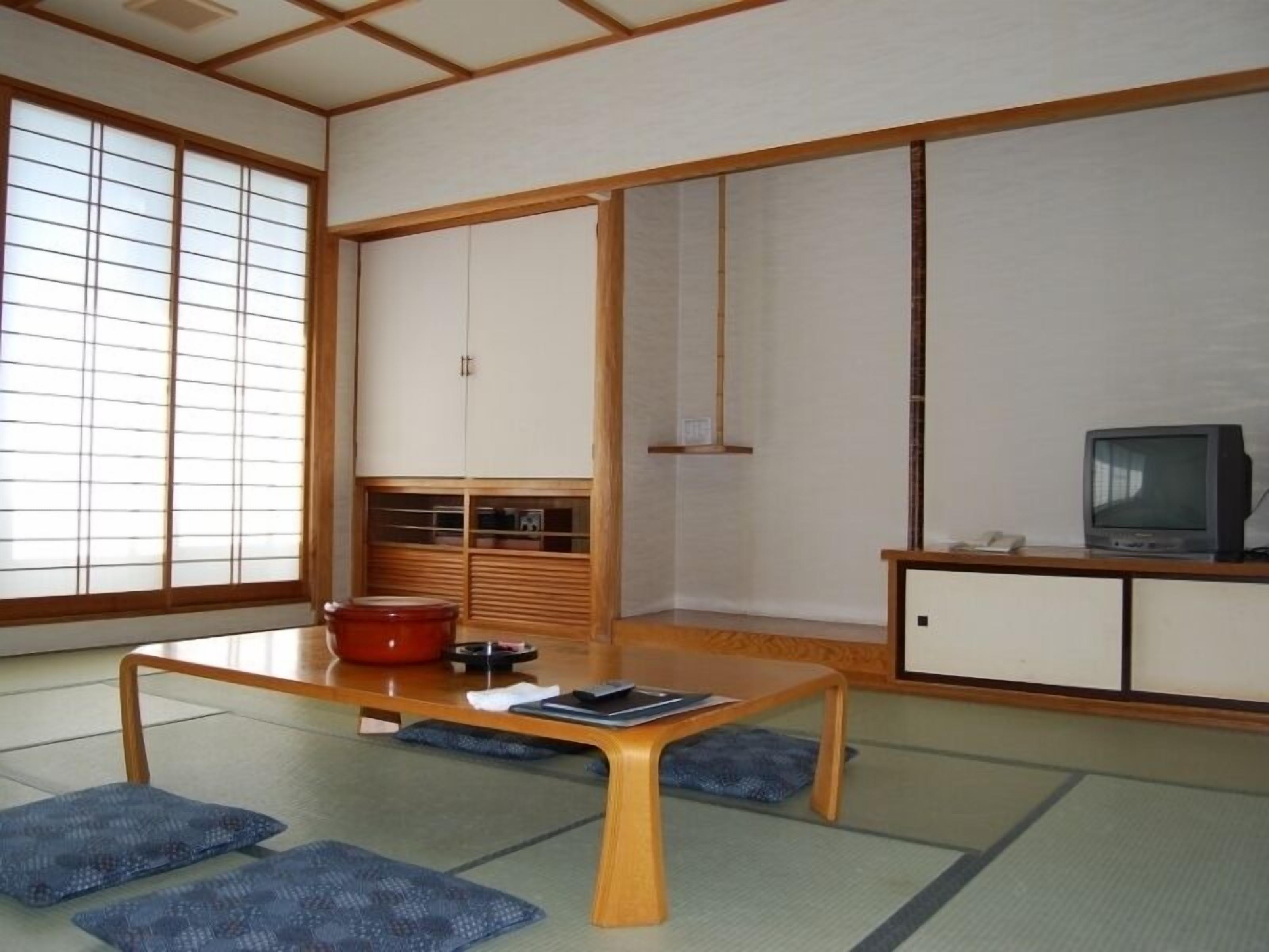 Una habitación japonesa tradicional con suelo de tatami, una mesa de madera baja, un televisor y puertas correderas.