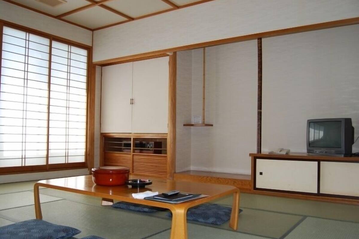 Une pièce de style japonais traditionnel, avec un sol recouvert de tatamis, une basse table en bois, un téléviseur et des portes coulissantes.