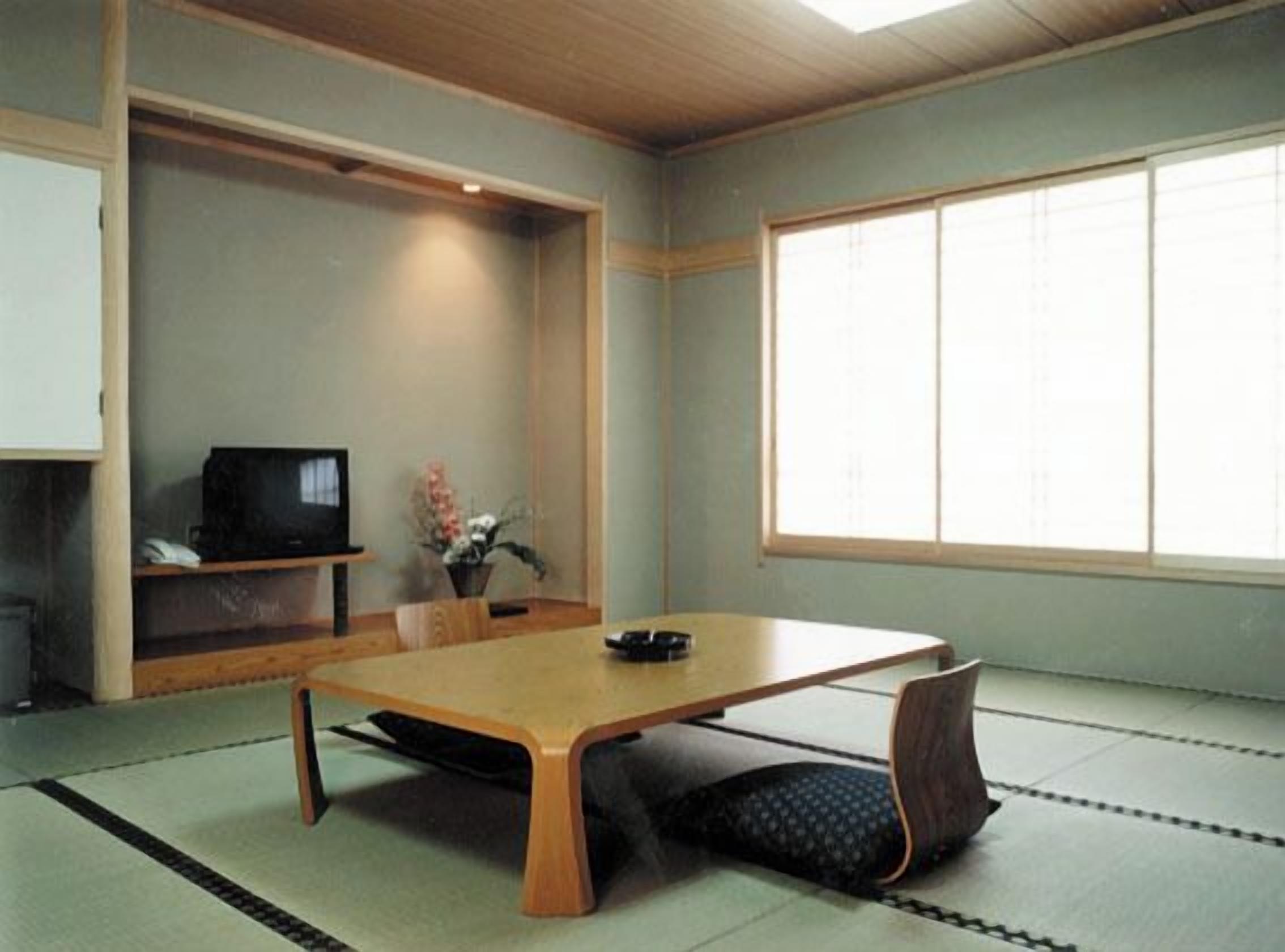 Una habitación japonesa tradicional con suelo de tatami, una mesa baja, un televisor y una ventana con celosías shoji.
