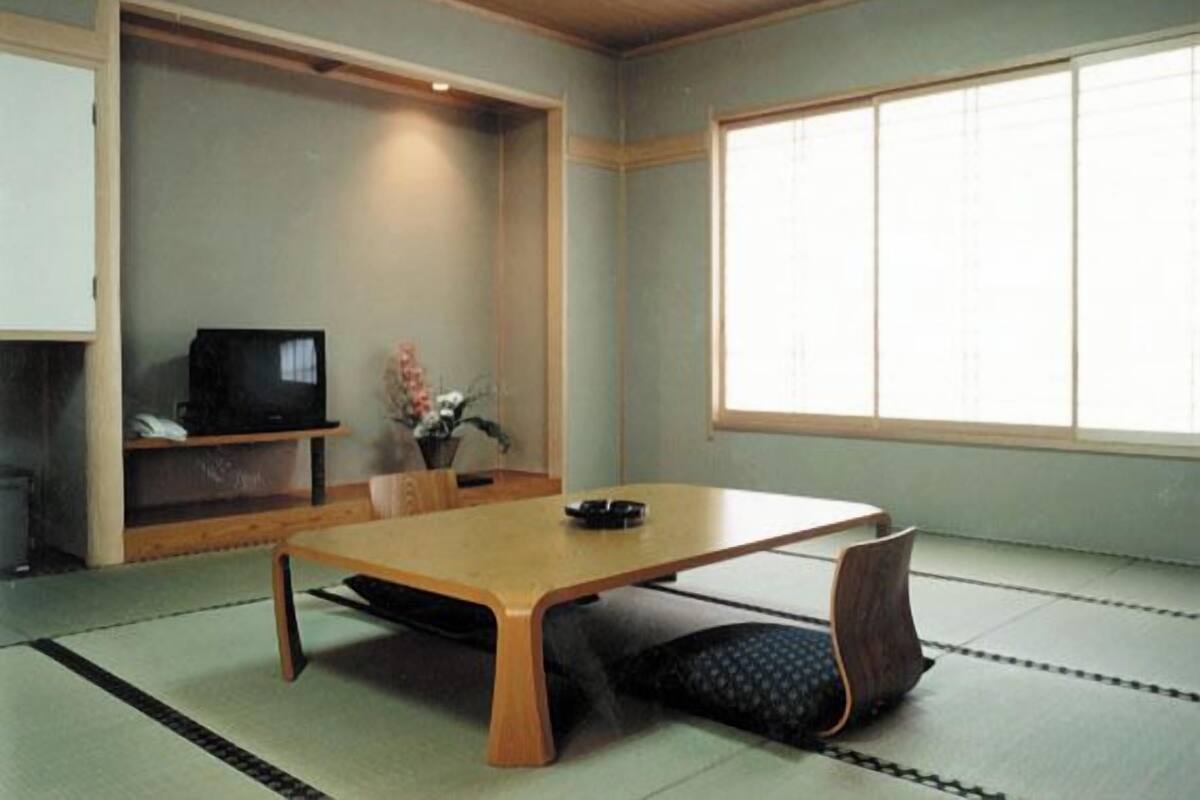 Une pièce de style japonais traditionnel, avec un sol recouvert de tatamis, une table basse, un téléviseur et une fenêtre dotée de panneaux coulissants en papier de riz (shoji).