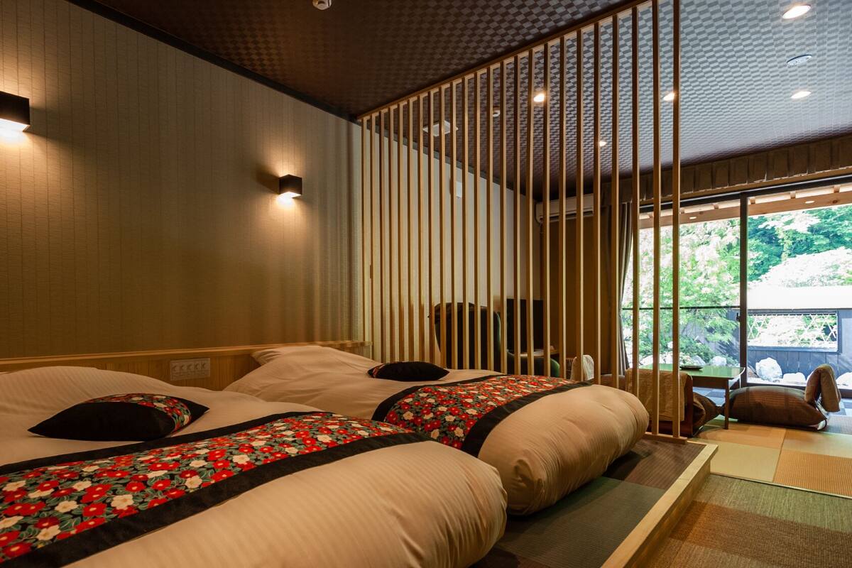 A hotel room with two beds, a sliding shoji screen, and a view of greenery outside.