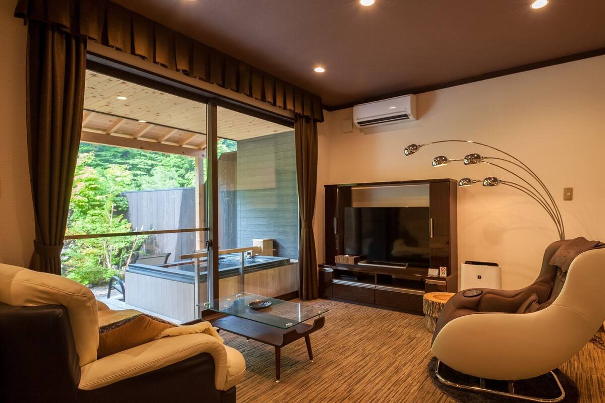 A modern living room with a glass table, sofa, and a massage chair.