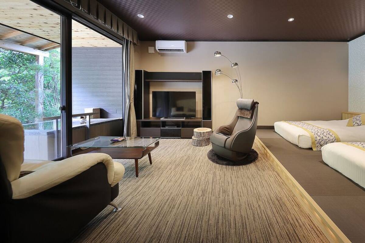 A modern hotel room with a sofa, a chair, a TV, and a bed.