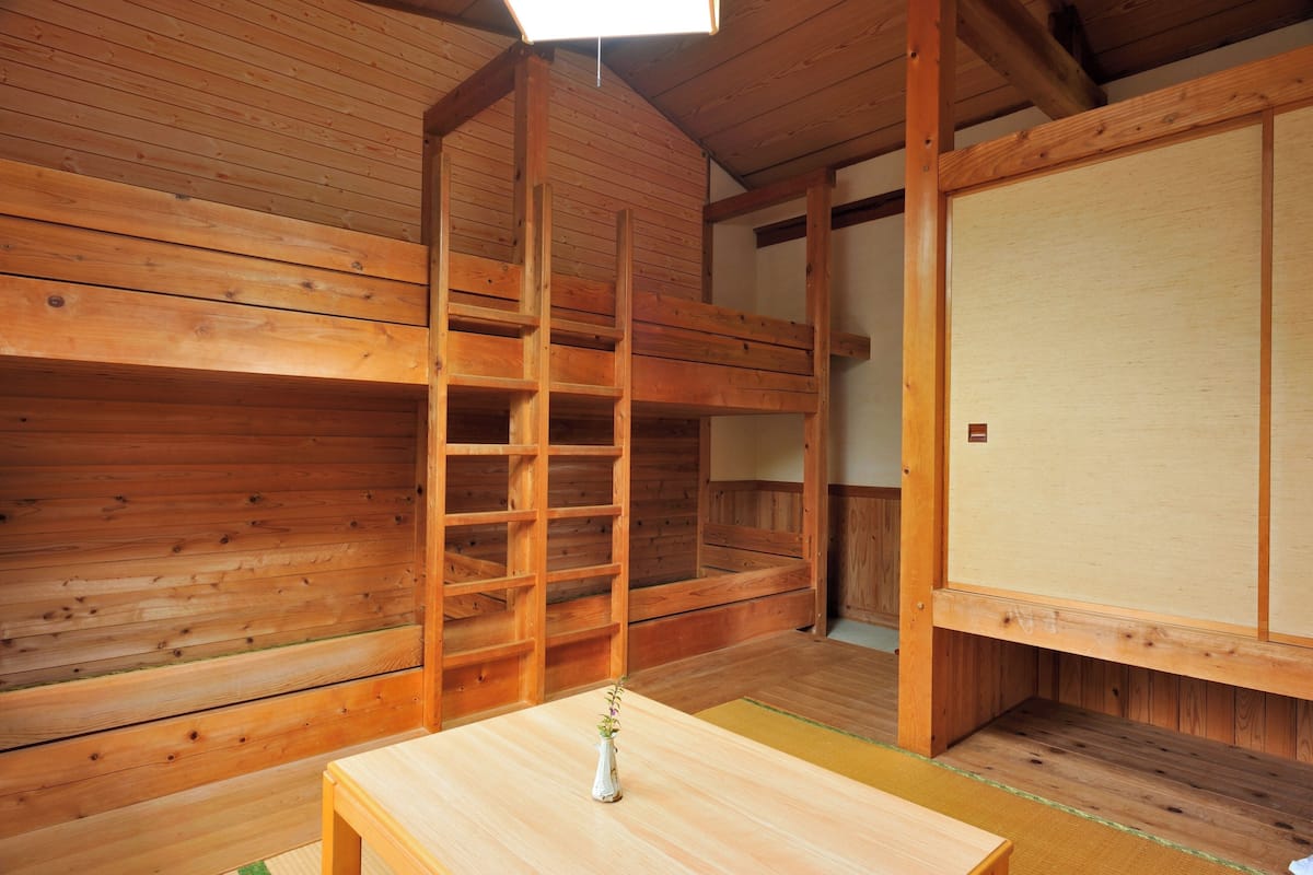 A wooden interior with bunk beds, a ladder, a small table with a vase, and a sliding door.