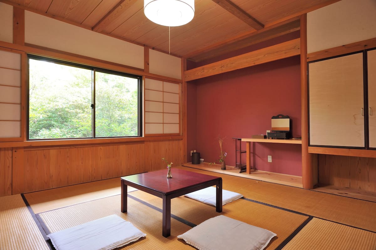 A traditional Japanese room with tatami flooring, a sliding door, a table with a vase, and a shelf with items.