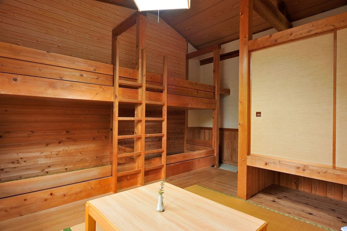A wooden room with a bunk bed, a small table with a vase, and a sliding door.