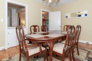 Une salle à manger avec une table et des chaises en bois, un miroir au mur et une porte donnant sur une autre pièce.