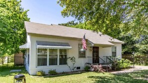 A single-story house with a front porch, a small front yard, and an American flag. - Mins to Ft Moore & Downtown - The Columbus Cottage (Columbus)