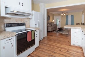 Une cuisine équipée d’une cuisinière, d’un four et de meubles blancs. On y trouve également un coin repas avec une table et des chaises.