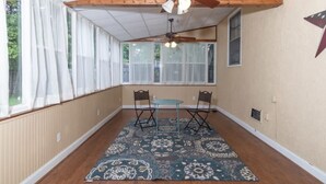 A room with a wooden floor, a patterned rug, a ceiling fan, a table with chairs, and large windows. - Mins to Ft Moore & Downtown - The Columbus Cottage (Columbus)