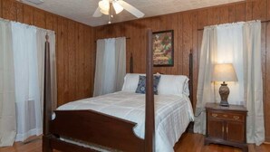 A four-poster bed with a wooden headboard, a nightstand with a lamp, and a painting on the wall. - Mins to Ft Moore & Downtown - The Columbus Cottage (Columbus)